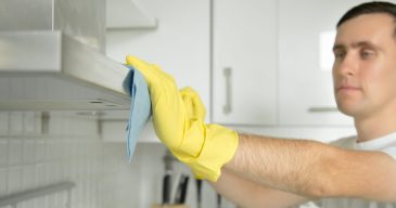 Closeup of male hands in rubber protective yellow gloves cleaning the kitchen metal extractor hood with rag. Home, housekeeping concept